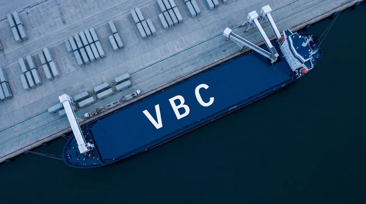 Aerial view of a cargo vessel at a container terminal, hatch covers marked VBC